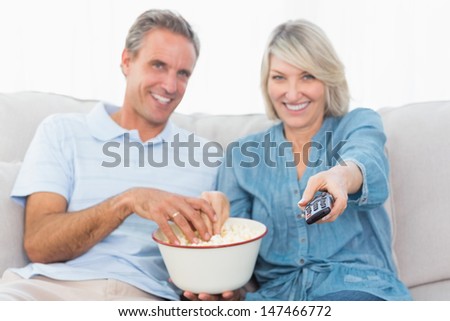 Couple watching tv and eating popcorn on the couch at home in living room