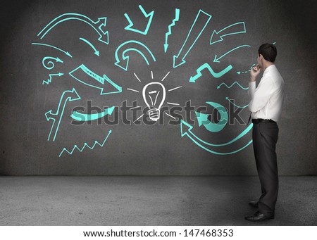 Businessman looking at a wall with drawings of arrows with a light bulb in the middle