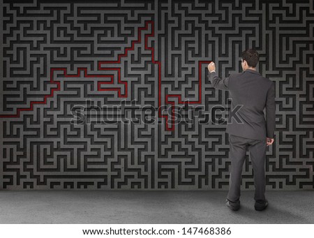 Rear view of a businessman drawing a red line through black maze on wall