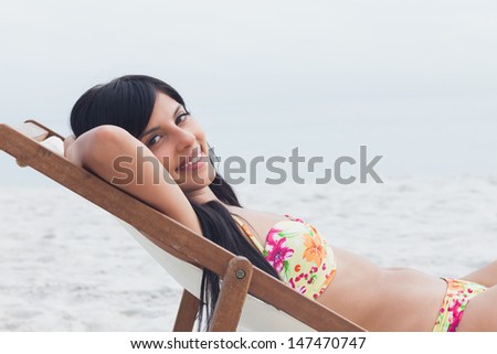Smiling woman resting on deck chair on beach