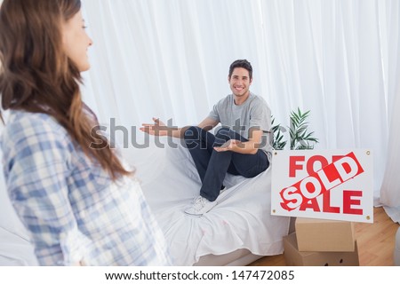 Man in his new house chatting with his wife next to a sign with sold written on it