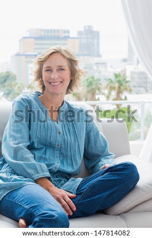 Happy blonde woman sitting on her couch smiling at camera at home in the sitting room