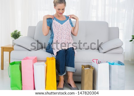 Blond woman with shopping bags trying out a top sitting on the sofa
