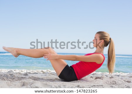 Fit blonde doing pilates core exercise on the beach