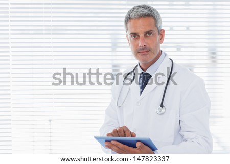 Doctor holding his tablet pc and looking at camera in medical office