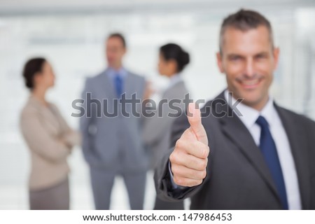 Smiling manager showing thumb up with employees in background in bright office
