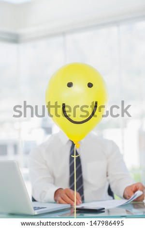 Yellow balloon with cheerful face hiding businessmans face in bright office