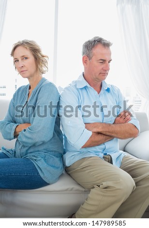 Middle aged couple sitting on the sofa not speaking after a fight with woman looking at camera at home in the living room