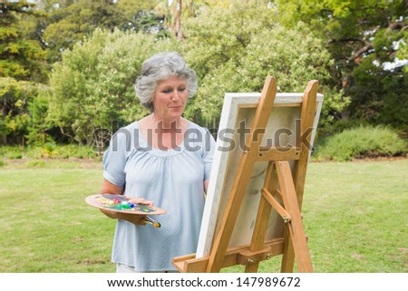 Happy mature woman painting on canvas in park