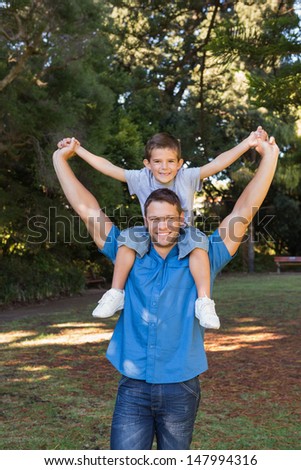 Father giving son piggy back and stretching out their arms smiling at camera in the park