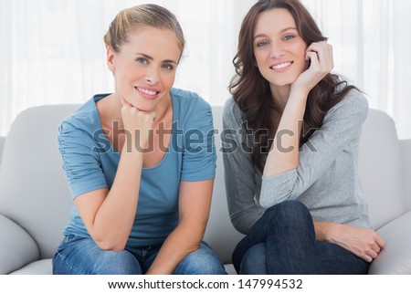 Two beautiful women posing while sitting on the couch and looking at camera