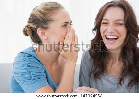 Woman telling secret to her friend and sitting on the sofa