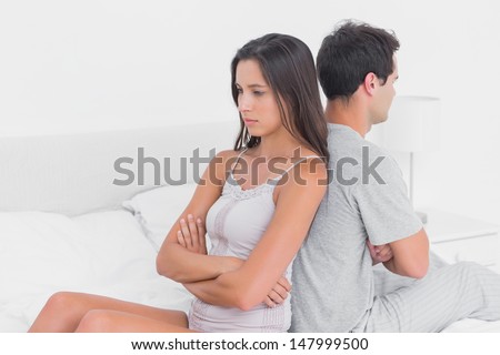 Unhappy couple ignoring each other sitting back to back on bed during a conflict