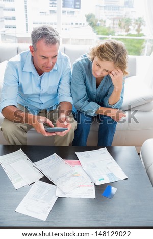 Middle aged couple sitting on their couch paying their bills at home in the living room