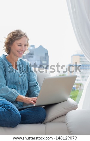 Smiling blonde woman sitting on her couch using laptop at home in the sitting room