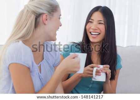 Young friends catching up over cups of coffee at home on couch