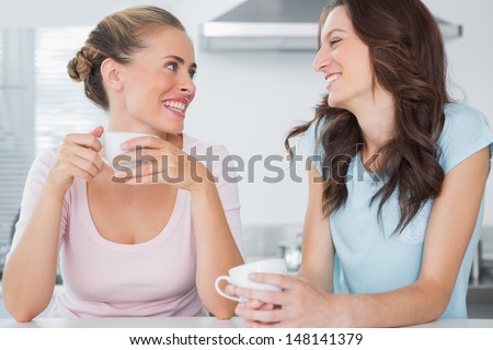 Laughing friends having cup of coffee in the kitchen