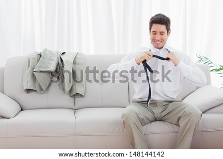 Smiling businessman sitting on sofa loosening his tie at home after long day