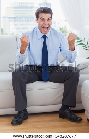 Victorious businessman cheering while sitting on sofa in cosy bright office
