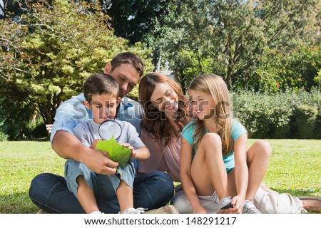 Happy family in a park with father and son inspecting leaf with magnifying glass on summers day