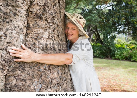 Happy older woman hugging a tree with closed eyes