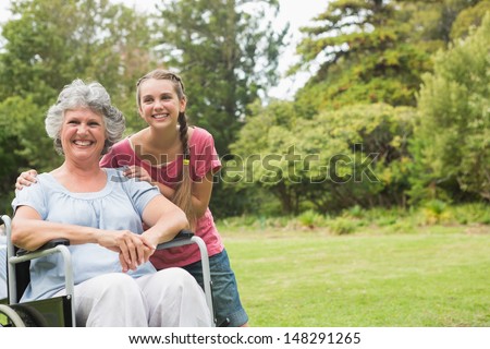Grandmother in wheelchair and granddaughter smiling into the camera in the park on sunny day