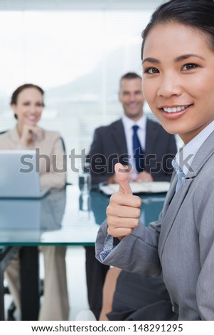Young pretty applicant in bright office showing thumb up after obtaining the job