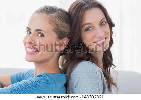 Cheerful women sitting back against back on the sofa