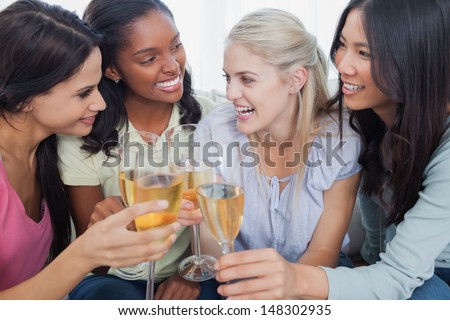 Friends toasting with white wine and smiling at home on couch
