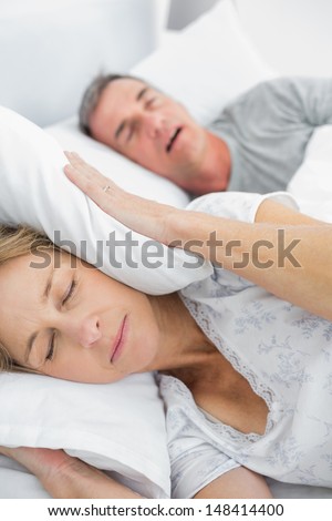 Tired Wife Blocking Her Ears From Noise Of Husband Snoring In Bedroom At Home