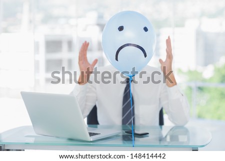 Blue balloon with sad face hiding angry businessmans face in bright office