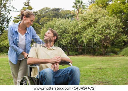 Smiling Man In Wheelchair Talking With Partner In The Park On Sunny Day