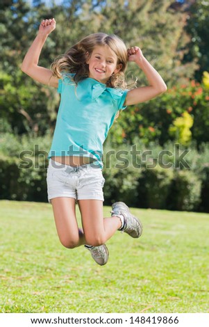 Cute girl jumping and smiling at camera in the park in sunshine