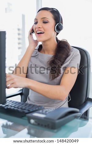 Attractive secretary in her office wearing headset and pointing at computer screen