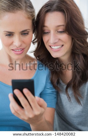 Smiling friends looking at mobile phone and sitting on the sofa
