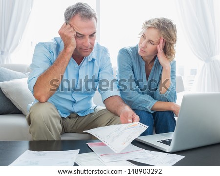 Worried couple using their laptop to pay their bills at home in the living room