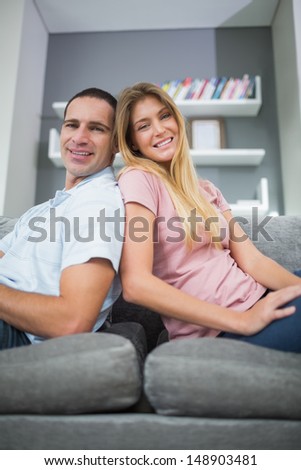 Happy couple sitting back to back on the couch together in sitting room at home