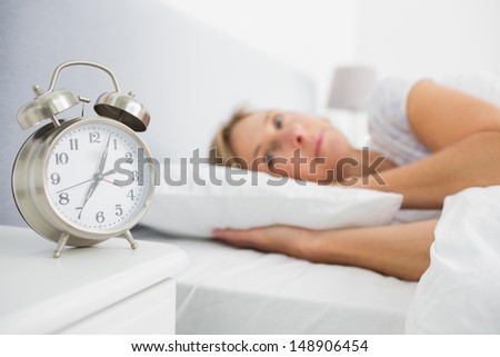 Blonde woman lying in bed while her alarm shows the early time at home in bedroom
