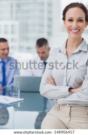 Cheerful businesswoman posing leaning against the desk in bright office