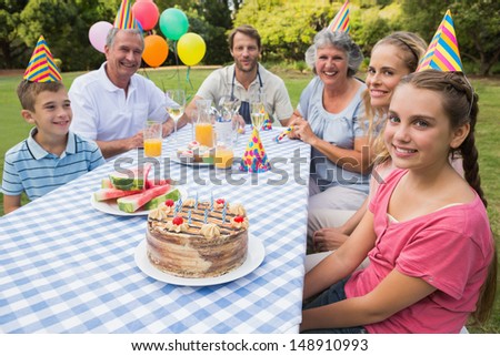 Extended family celebrating little girls birthday outside at picnic table smiling at camera