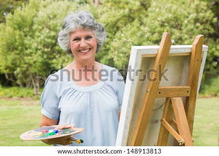 Happy mature woman painting on canvas and looking at camera in the park