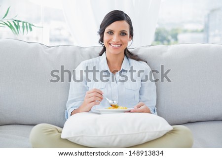 Pretty woman sitting on the couch crossing legs eating fruits in her living room