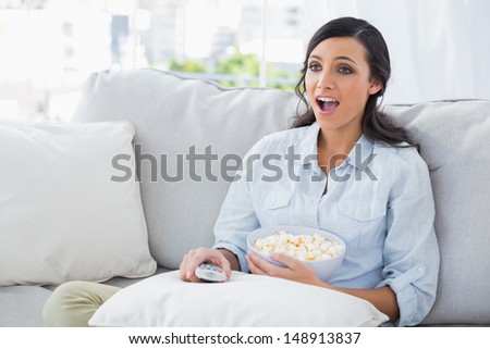 Astonished woman relaxing on the sofa eating popcorn in her living room