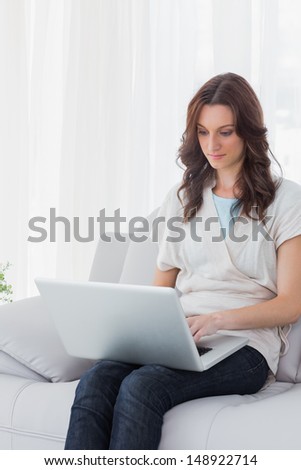 Concentrated woman with laptop on her knees and sitting on the couch