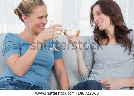 Happy women looking at each other clinking their wine glasses while sitting on the sofa