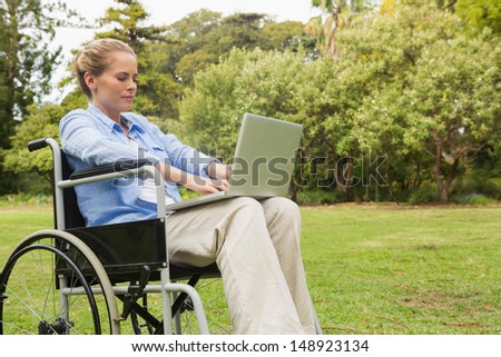 Young woman in the park using a laptop in her wheelchair