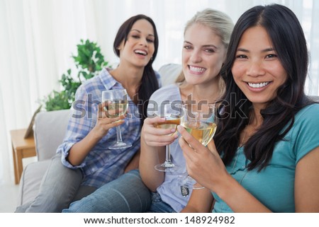 Happy friends having white wine together looking at camera at home on couch