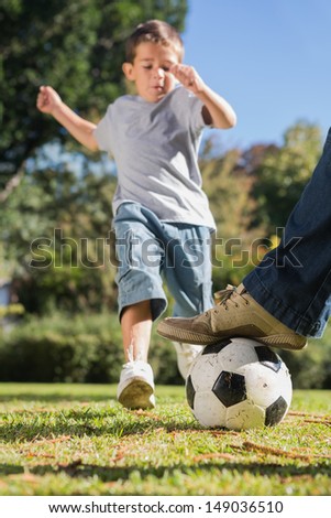 Boy kicking the football from under dads foot in the park