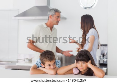 Unhappy Siblings Sitting In Kitchen With Their Parents Who Are Fighting At Home Loudly