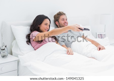 Woman changing tv channel in her bed with her husband